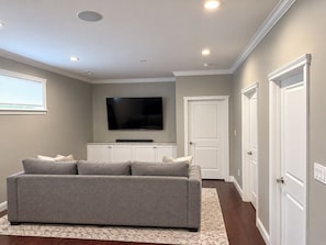 A living room with a grey sofa, a flat-screen TV, a cabinet, and a patterned rug.