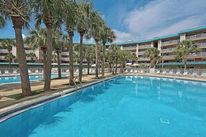 A swimming pool surrounded by palm trees and a hotel building with multiple balconies. - 3BR Gulf Views | 2 Pools | Beach Access | Miramar Beach (Miramar Beach)