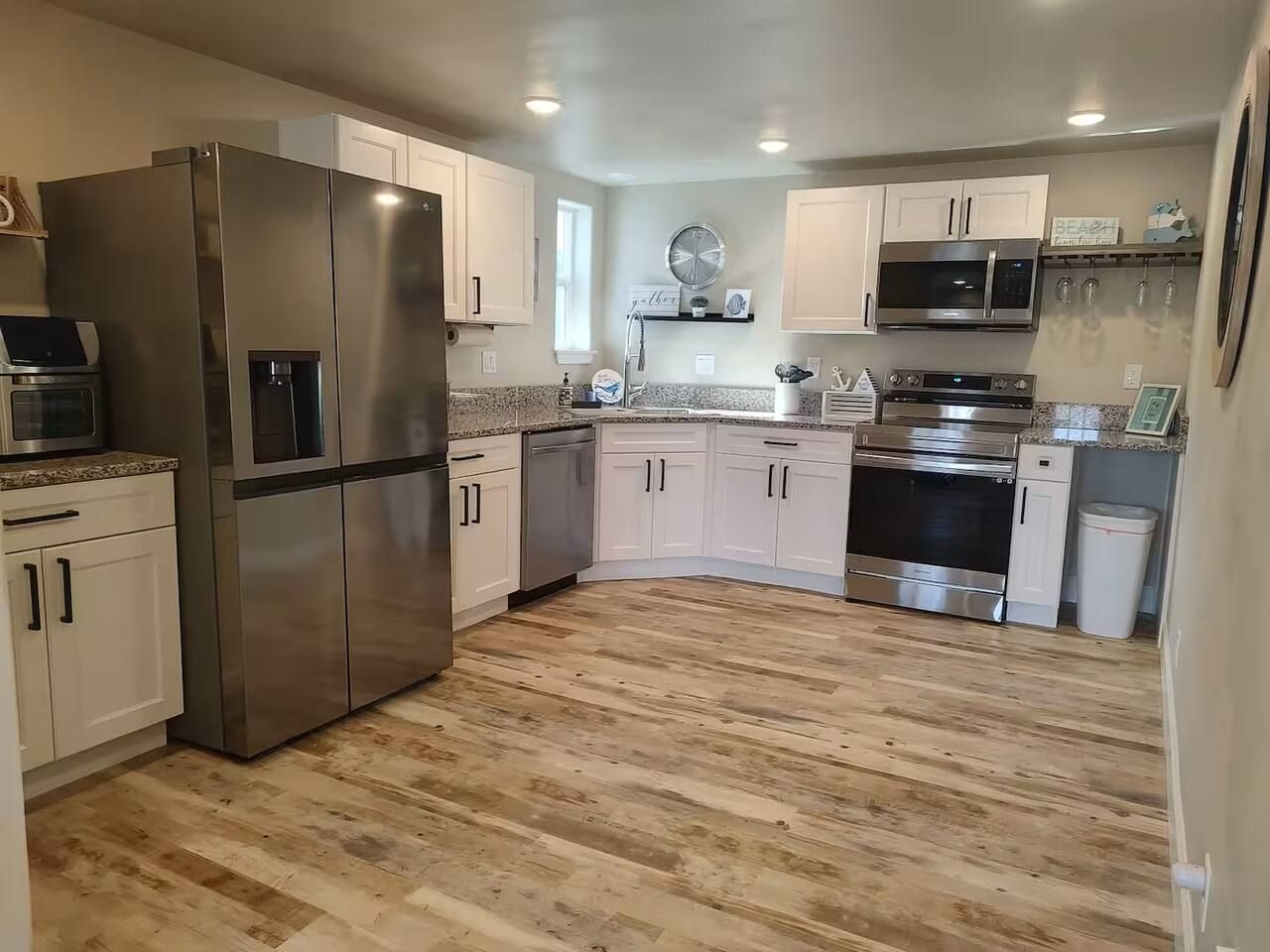 A modern kitchen with stainless steel appliances, white cabinetry, and a wooden floor.