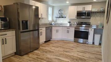 A modern kitchen with stainless steel appliances, white cabinetry, and a wooden floor.