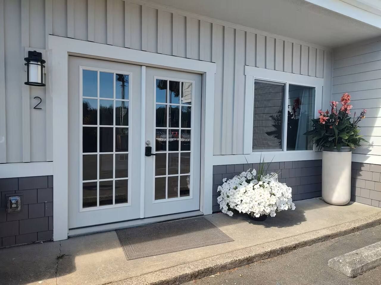 A house with a white exterior, a double door with glass panels, a small window, and a potted plant with white flowers.
