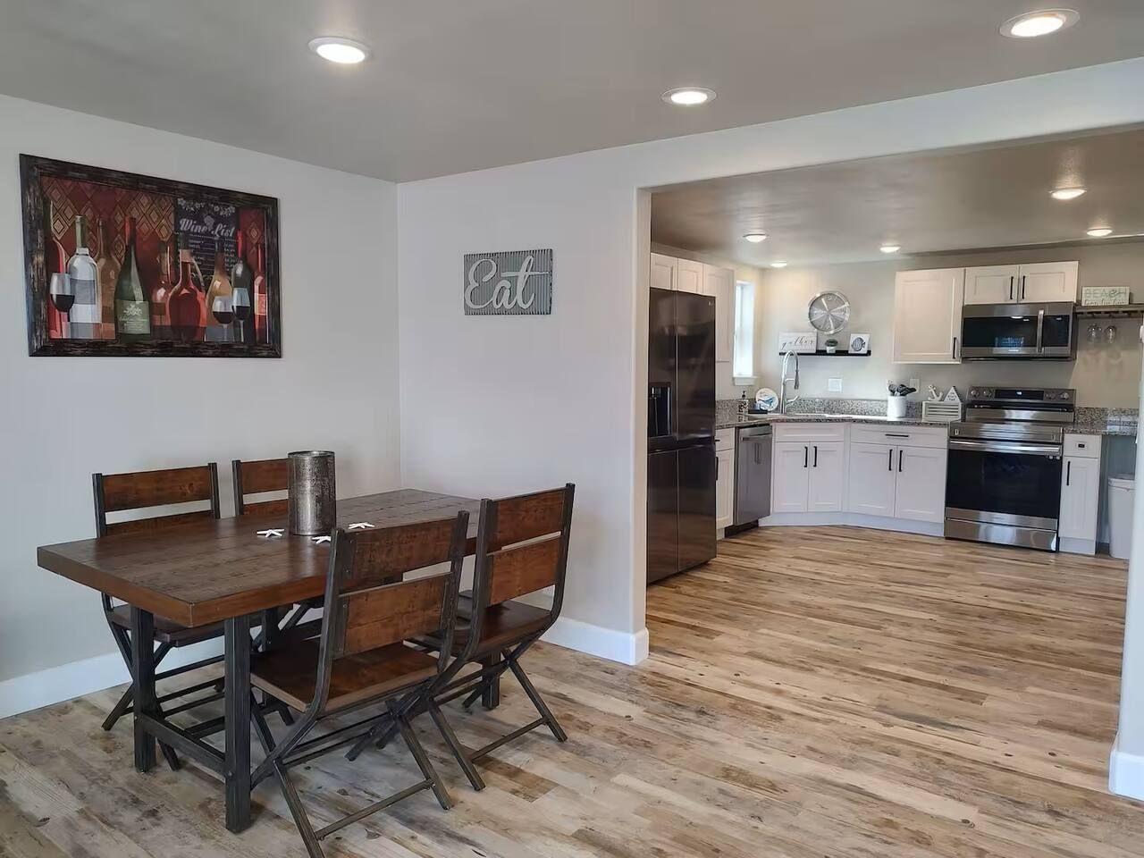 A dining area with a wooden table and chairs, a kitchen with stainless steel appliances, and a wooden floor.