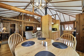 A wooden interior with a round dining table, chairs, a ceiling fan, and a television. - Cedar Crest Cabin: Autumn Views on the Manistee River | Cozy Cabin Getaway (Grayling)