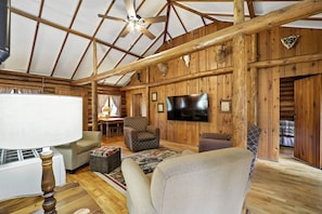 Ein rustikales Cabin-Interieur mit Holzbalkendecke, einem an der Wand montierten Fernseher und einer gemütlichen Sitzecke mit einem gemusterten Teppich.