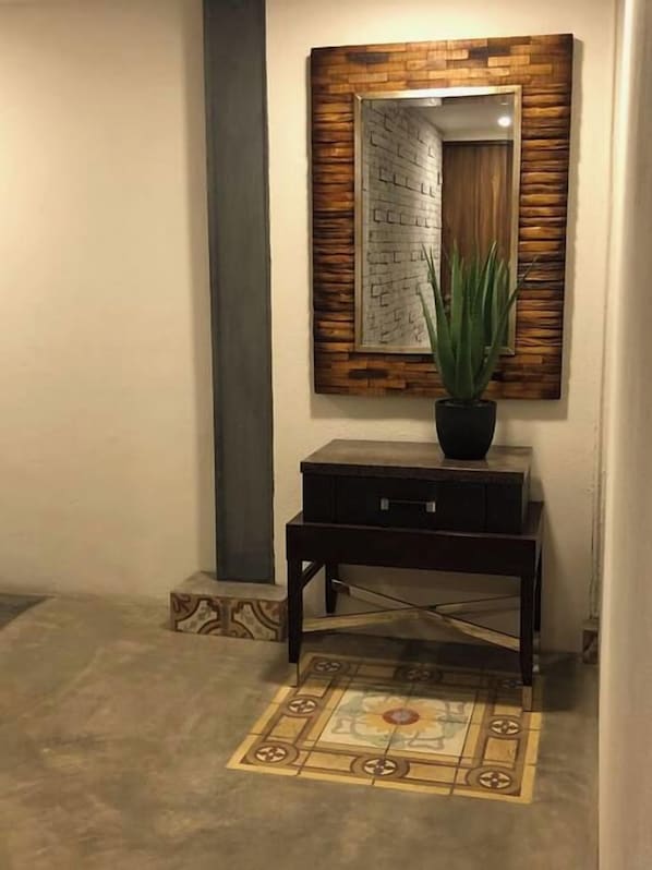 Een gang met een houten console tafel, een potplant, een kamerkleed met patroon en een spiegel met houten lijst.