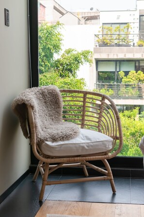 A wicker chair with a cushion and a fluffy throw, positioned by a window with a view of buildings and greenery. - Increible Terraza en la condesa (Ciudad de México)