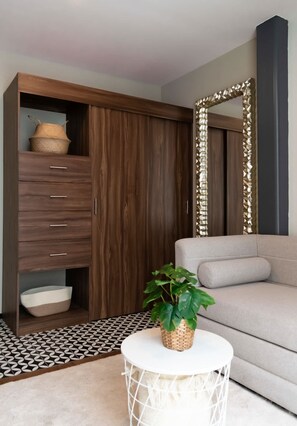 Ein modernes Wohnzimmer mit einer Couch, einem runden weißen Beistelltisch, einem Topf mit Pflanze, einem Holzschrank mit Schubladen und einem dekorativen Spiegel.