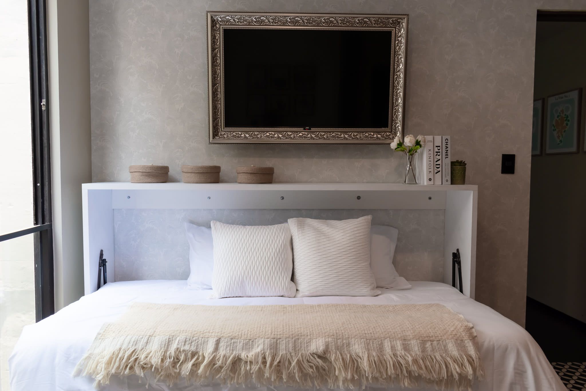 Una cama con ropa blanca, un cabecero blanco y un espejo decorativo encima.