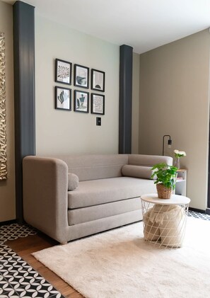 A modern living room with a sofa, a rug, a small round table with a plant, and framed artwork on the wall. - Increible y acogedor departamento en la condesa (Ciudad de México)