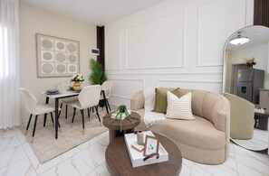 A modern living room with a beige sofa, a round coffee table, and a dining area with a white table and chairs. - Elegant and Modern Apartment in Bayahíbe | Near the Beach (Bayahíbe)