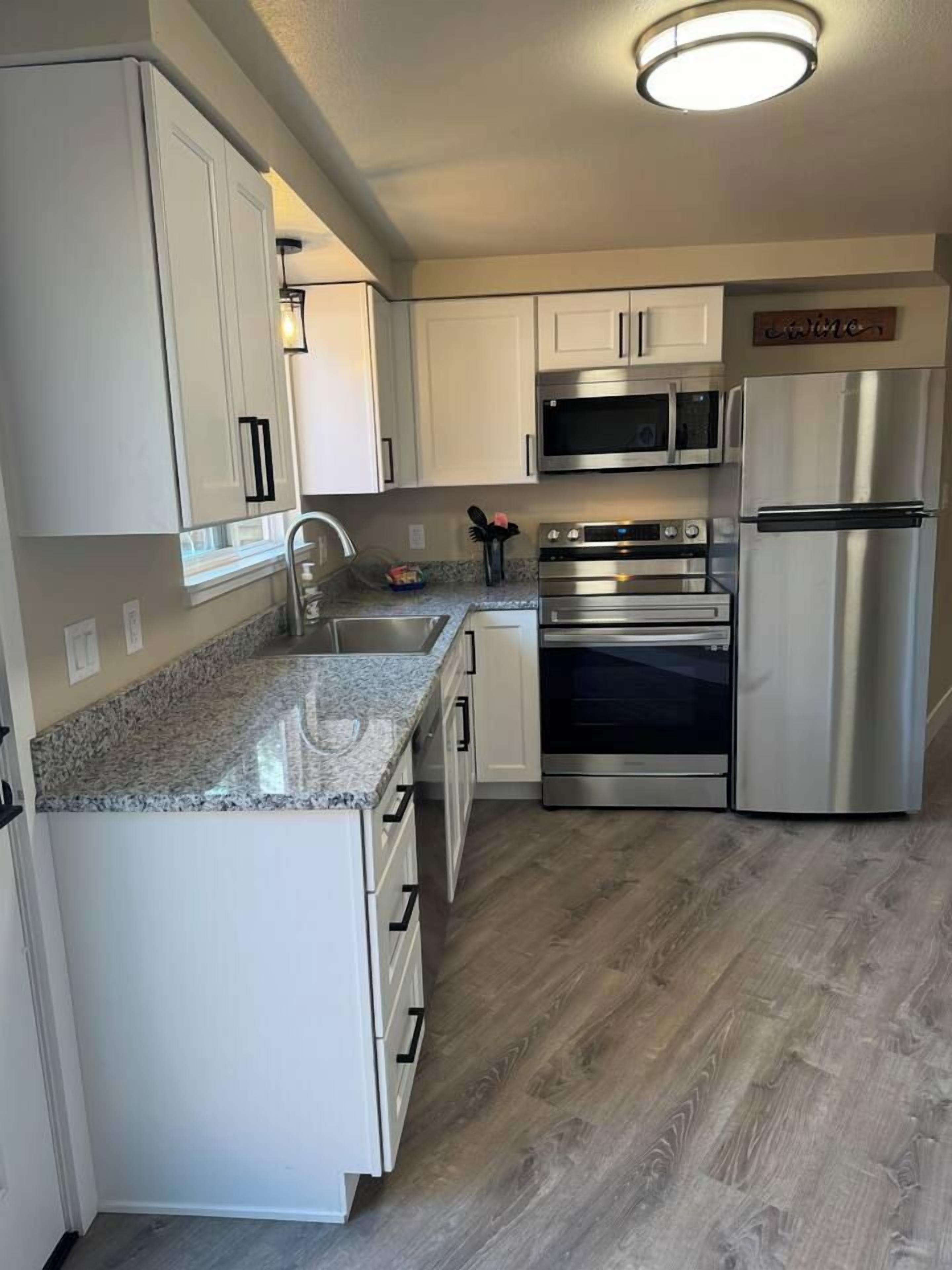 A kitchen with white cabinets, a granite countertop, stainless steel appliances, and a wooden floor.