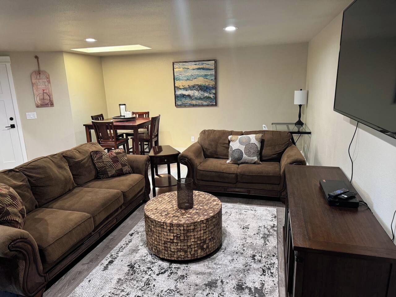 A living room with a brown sofa, a round coffee table, a TV, and a painting on the wall.