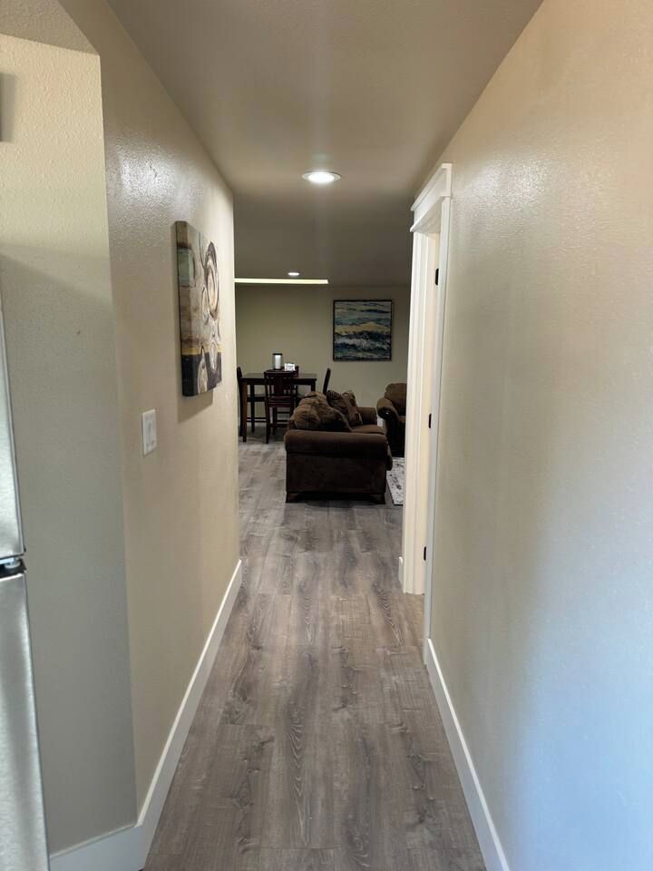 A hallway with a wooden floor leading to a living area with a couch and a painting on the wall.