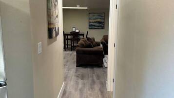 A hallway with a wooden floor leading to a living area with a couch and a painting on the wall.