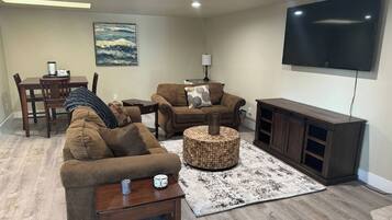 A living room with a sofa, ottoman, coffee table, TV, and a dining area with chairs and a table.