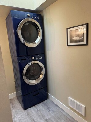 A stacked washer and dryer unit in a corner of a room with a beige wall and a framed picture. - Fun Florence 2 BR, close to all. Unit 4 (Florence)