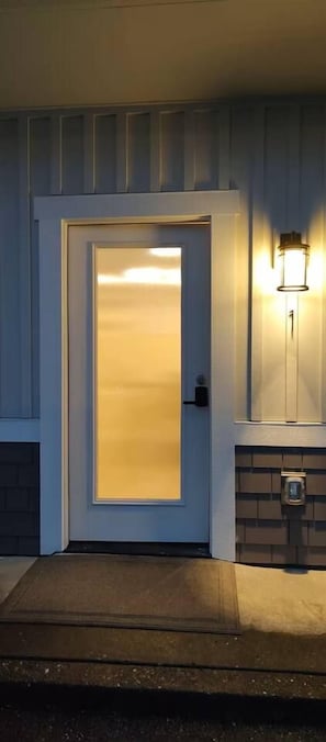 A front door with a frosted glass panel, a wall-mounted light fixture, and a doormat. - Old Town Florence Getaway 2 BRM, Unit 1 (Florence)