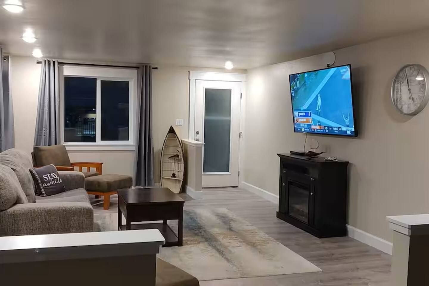 A living room with a sofa, a coffee table, a television, and a clock on the wall.