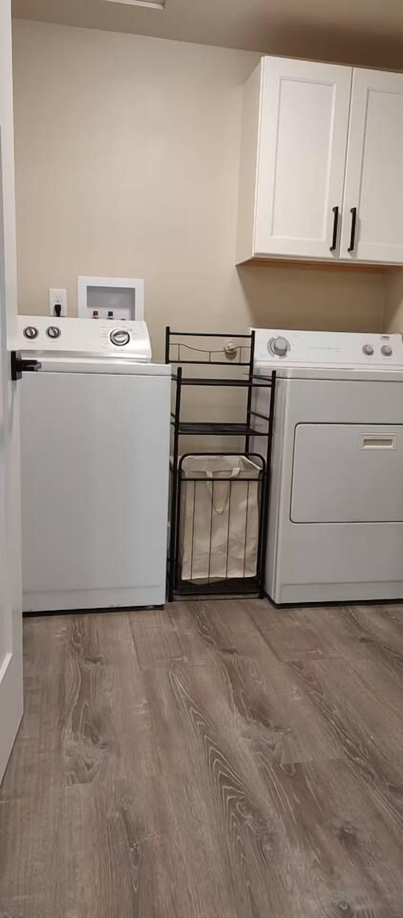 A laundry room with two washing machines, a drying rack, and a cabinet.
