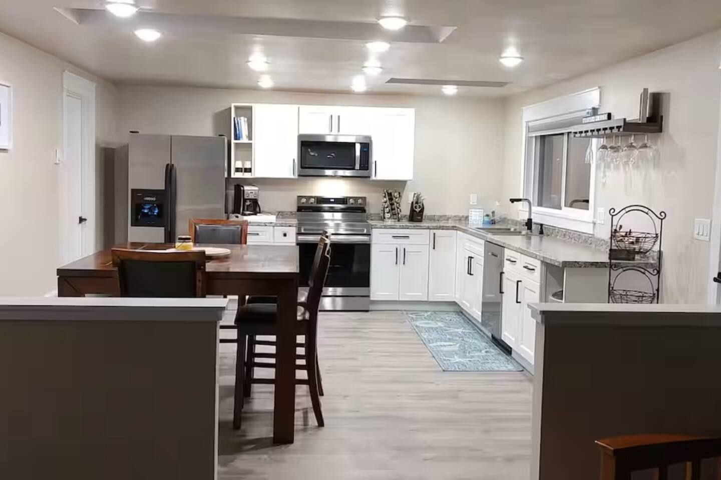A modern kitchen with white cabinetry, stainless steel appliances, and a dining area with a wooden table and chairs.
