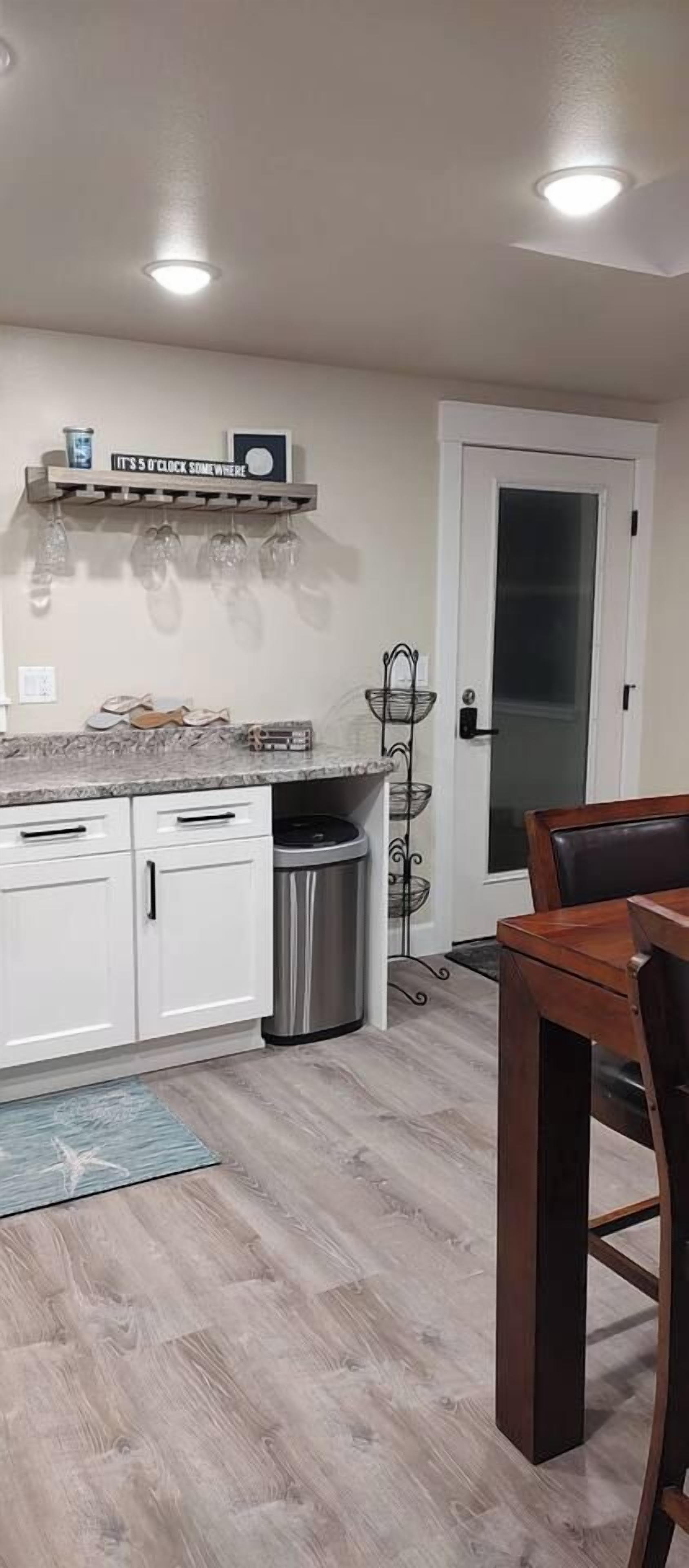 A kitchen with white cabinets, a stainless steel trash can, and a wooden dining table.