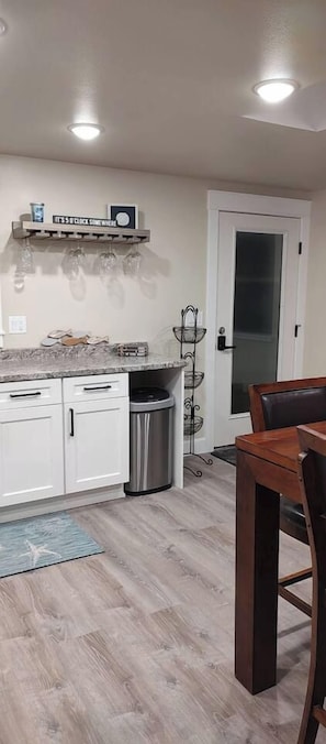 A kitchen with white cabinets, a stainless steel trash can, and a wooden dining table. - Old Town Florence Getaway 2 BRM, Unit 1 (Florence)