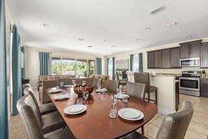 Ein Essbereich mit einem großen Tisch für sechs Personen, eine Küche mit modernen Geräten und ein Wohnbereich mit einer Couch und einem Fernseher.