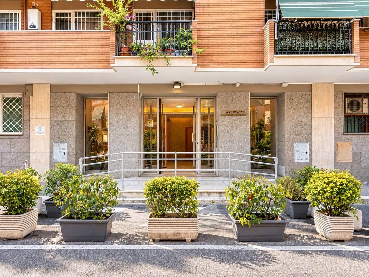 A hotel entrance with a glass door, potted plants, and a balcony with a railing.