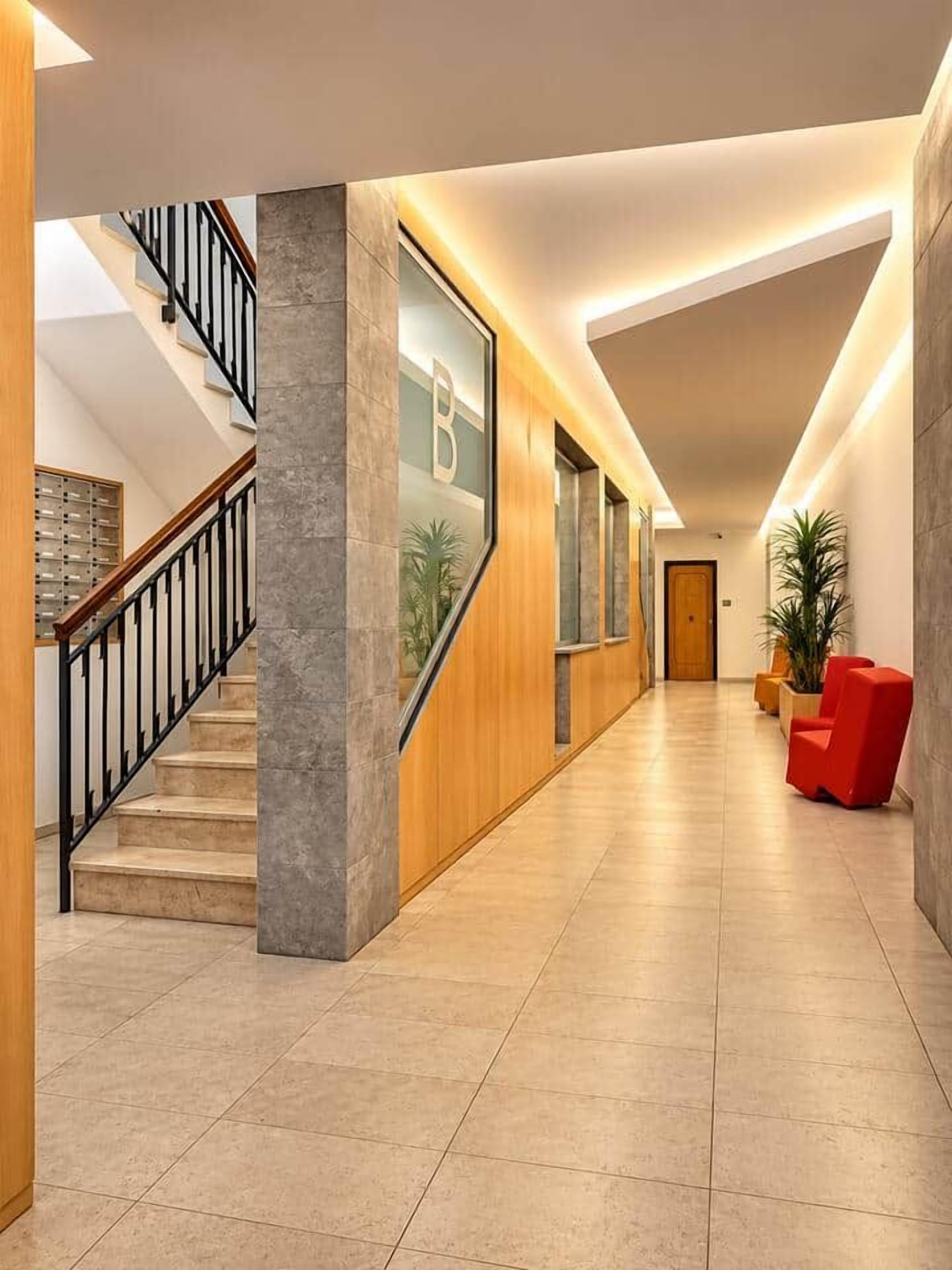 Eine moderne Hotelhalle mit Treppe, einer Rezeption und einem roten Sessel.