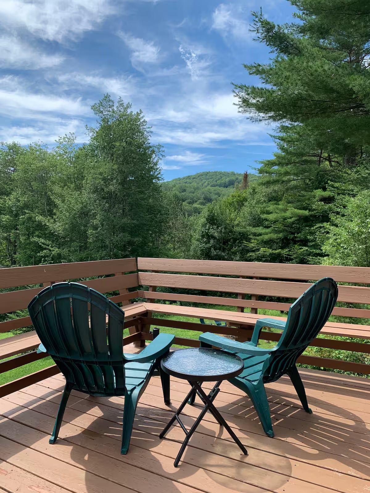Une terrasse en bois avec une table et deux chaises, entourée d’une clôture en bois et d’une végétation luxuriante.
