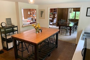 Ein Essbereich mit Holztisch, Stühlen und einem Blumenstrauß. Im Hintergrund sind ein Bücherregal und ein Fenster zu sehen.