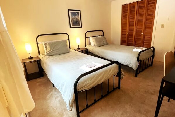 A bedroom with two single beds, bedside tables, a wardrobe, and a chair.