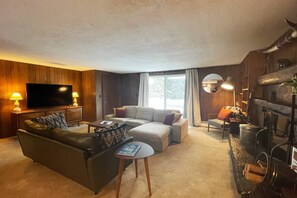 A living room with a flat-screen TV, leather sofas, a coffee table, and a fireplace with a stone mantle. - The Rose Lodge: 8 Bedrooms, 7 Baths, Private Hot Tub and Game Room (Killington)
