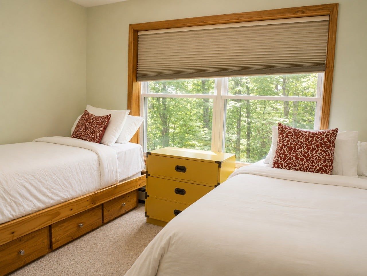 A bedroom with two beds, a wooden nightstand, and a window with a view of trees.