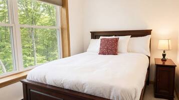 A bedroom with a large bed, a nightstand, a lamp, and a window with a view of trees.