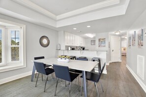 A modern kitchen with white cabinets, a marble countertop, and a dining area with a white table and black chairs. - Ocean-view 3BR condo with pool accces (Tybee Island)