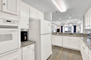 A modern kitchen with white cabinetry, a built-in coffee maker, and a granite countertop. - Ocean-view 3BR condo with pool accces (Tybee Island)