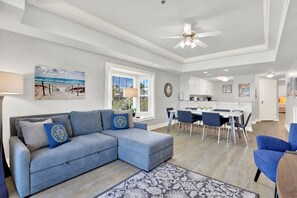 A modern living room with a sectional sofa, dining area, and kitchen. - Ocean-view 3BR condo with pool accces (Tybee Island)