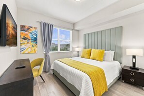 A modern bedroom with a bed, bedside tables, a desk, a chair, and artwork on the walls. - From Convention Days to Park Days, 3BR Condo (Orlando)