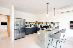 A modern kitchen with a large refrigerator, a microwave, a stove, and a sink. There are two bar stools and a pendant light. - Cozy 1-bedroom apartment in beautiful Tamarindo with AC (Tamarindo)