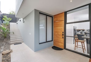 A modern interior with a staircase leading to a second floor, a glass door with a wooden panel, and a kitchen area visible through the glass. - Cozy 1-bedroom apartment in beautiful Tamarindo with AC (Tamarindo)
