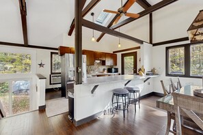 A modern kitchen with a large island, wooden beams, and a view of the outdoors. - Riverview Retreat | beach, float, ski (Campton)