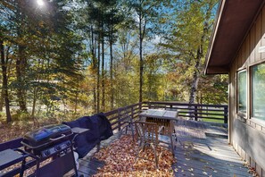 An outdoor deck with a grill, a table, and chairs, surrounded by trees and a wooden fence. - Riverview Retreat | beach, float, ski (Campton)