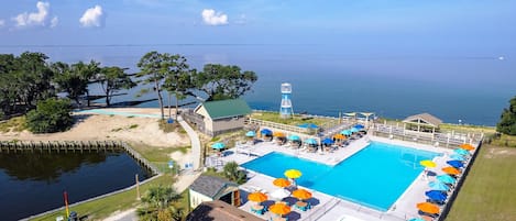A pool area with a view of the ocean, a lifeguard tower, and a beach with trees.