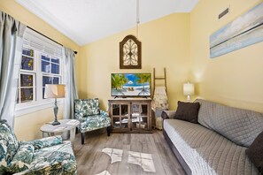 A cozy living room with a sofa, armchair, and a television on a wooden cabinet. - 5519 Moffitt's, Sound Side, Community Pool/Tennis (Kill Devil Hills)