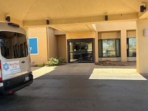 A parking area with a white van parked in front of a building with a glass door entrance. - SureStay (Oklahoma City)