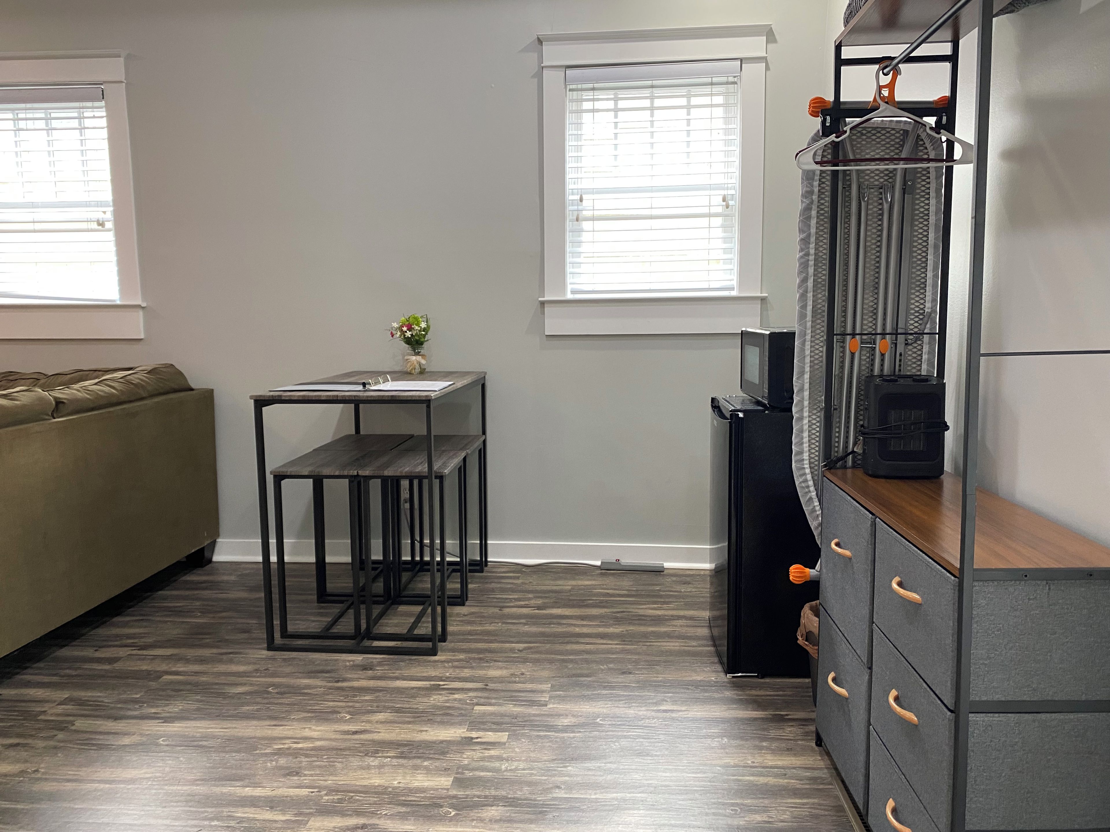 A compact living space with a sofa, a small table with a vase, a microwave, and a cabinet with drawers.