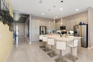 A modern kitchen with a central island, stainless steel appliances, and pendant lighting. - Luxury Solterra Resort 10BR w/ Pool & Movie Room (Davenport)