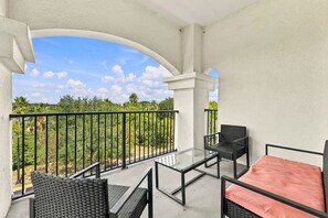 Ein Balkon mit Glastisch, zwei Stühlen und einer Couch mit Kissen.