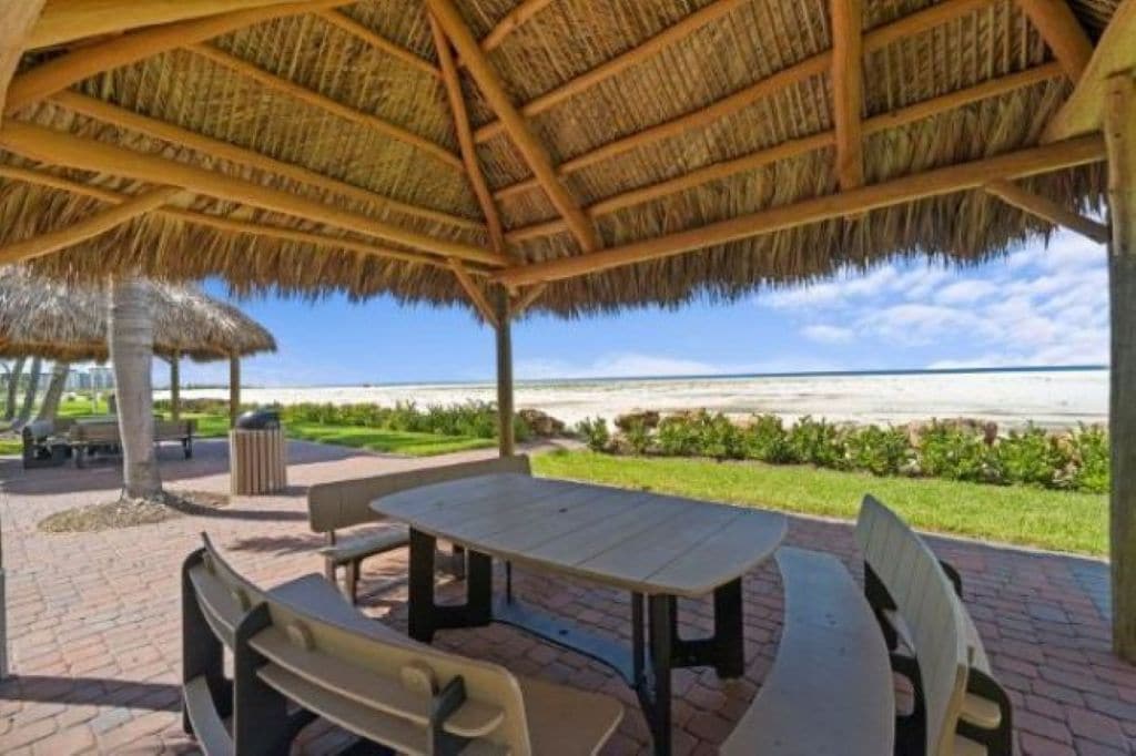 A covered outdoor seating area with a table and benches, overlooking a beach.